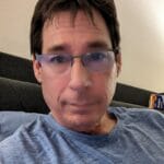 Man wearing glasses and gray shirt sits on couch